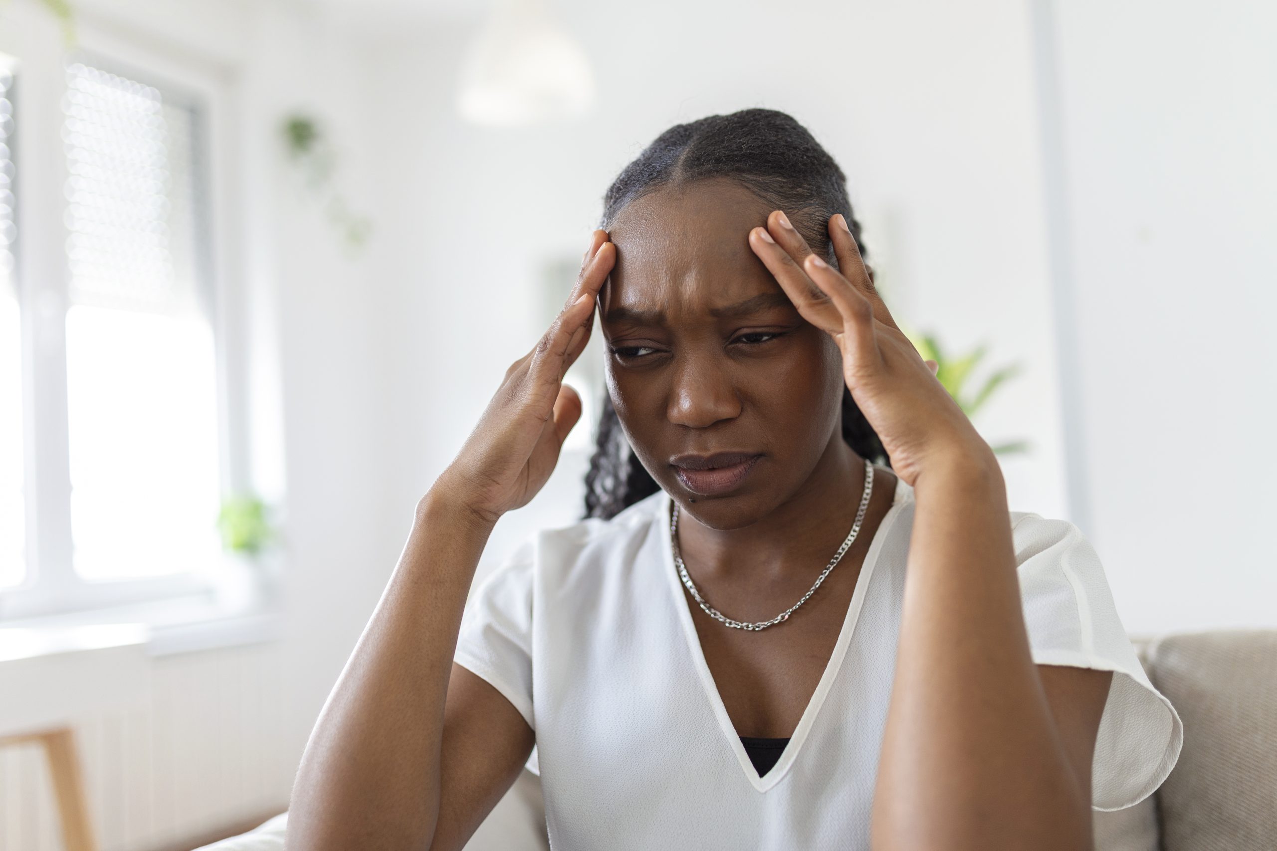 Young woman sitting on a couch holding her head, looking tired and frustrated